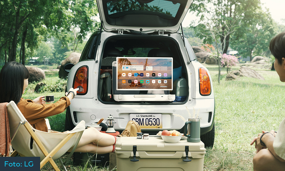 Ein Fernseher steht im Kofferraum eines Autos und Personen sitzen davor und schauen zu.