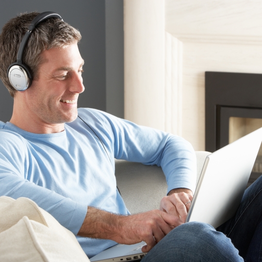 Eine Person hört Radio über Kopfhörer, während sie auf einem Laptop arbeitet.