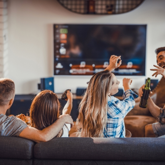 Vier Personen lachend vorm Fernseher. 