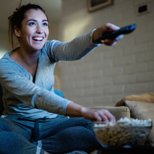 Lachende Frau mit Fernbedienung und Popcorn.