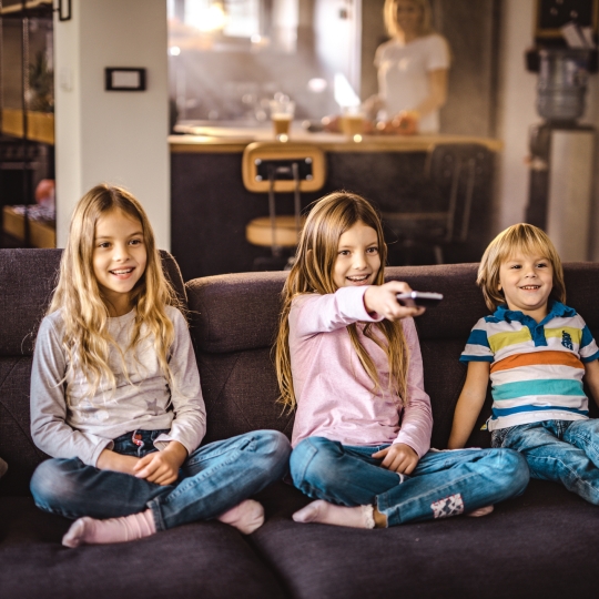 Glückliche Kinder mit Fernbedingung in der Hand auf einer Couch.