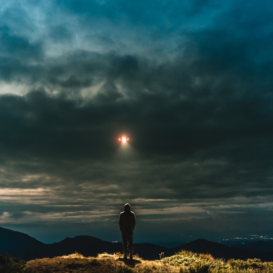 Eine Person auf einem Berg, die von einem UFO angeleuchtet wird. 