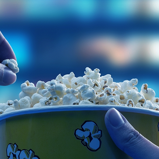 Eine Hand greift in einen großen Kübel Popcorn.