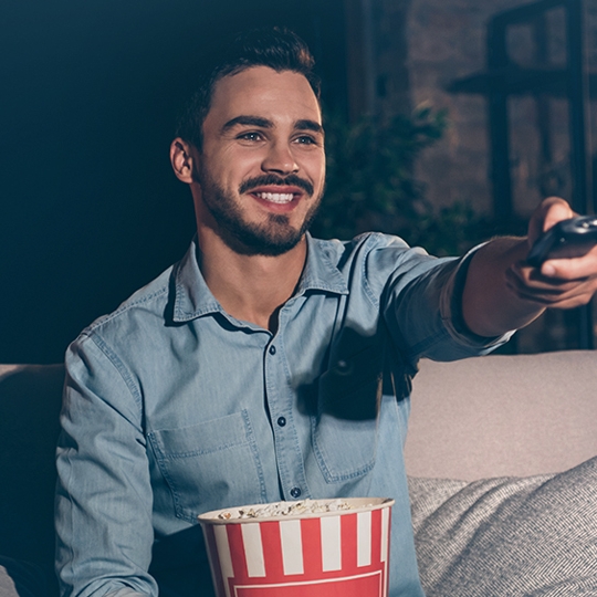 Person lächelt und hält eine Fernbedienung Richtung Fernseher.