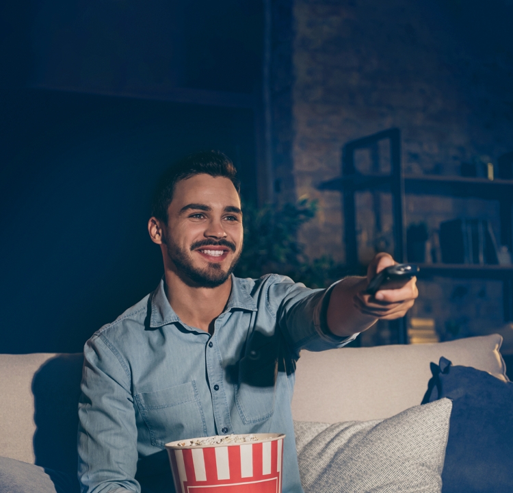 Eine Person hält lächelnd eine Fernbedienung in Richtung Fernseher.
