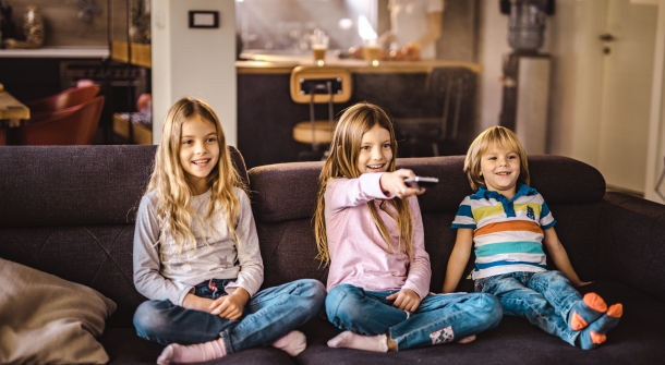 Glückliche Kinder mit Fernbedingung in der Hand auf einer Couch.
