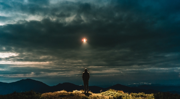 Eine Person auf einem Berg, die von einem UFO angeleuchtet wird.